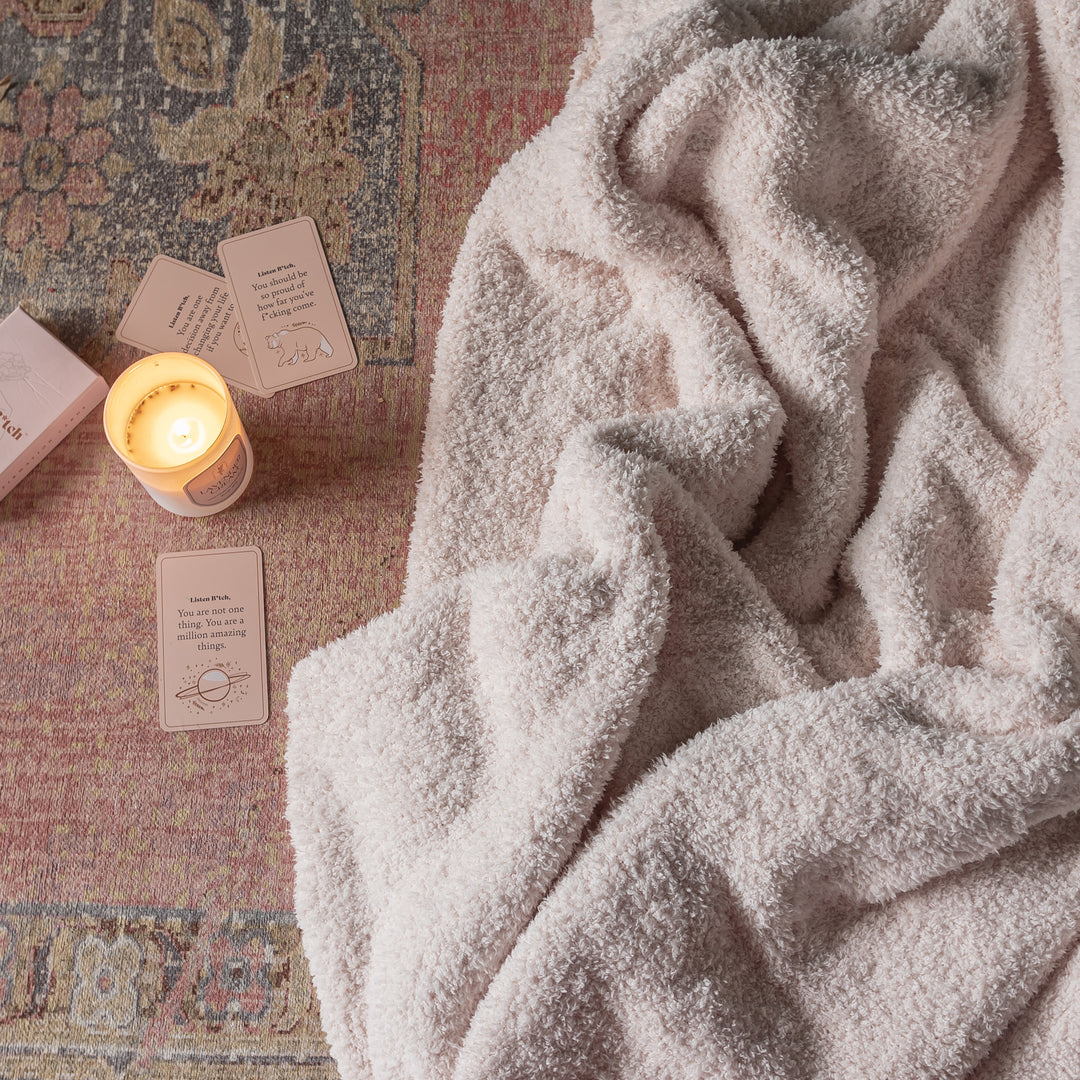 Cozy blanket draped over a textured surface with a lit candle and cards.