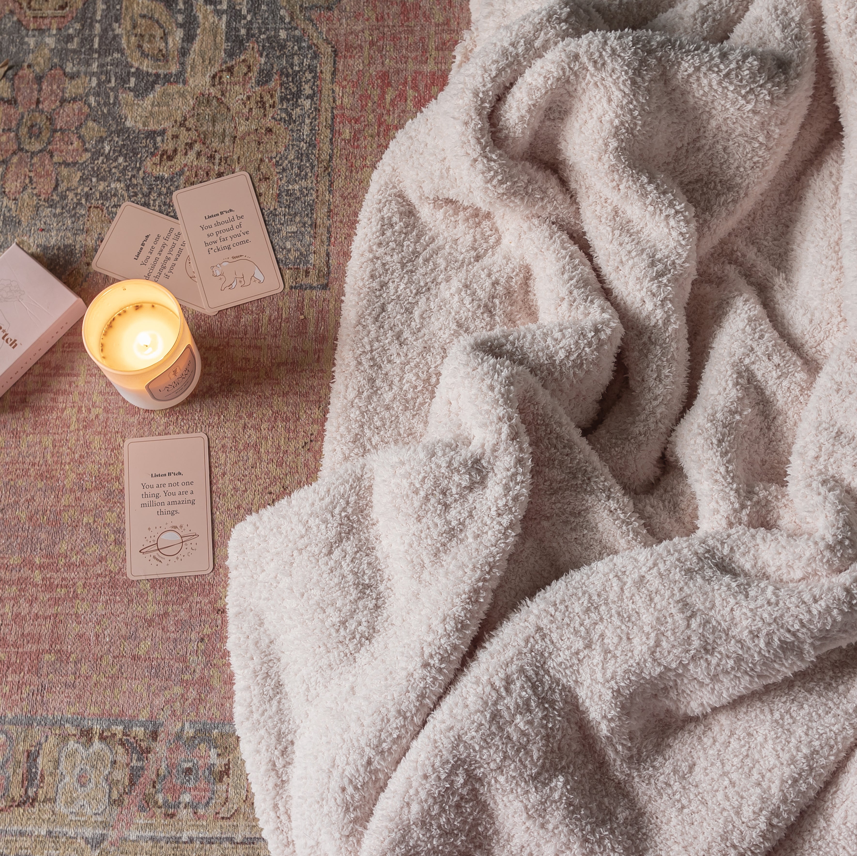 Cozy blanket draped over a textured surface with a lit candle and cards.