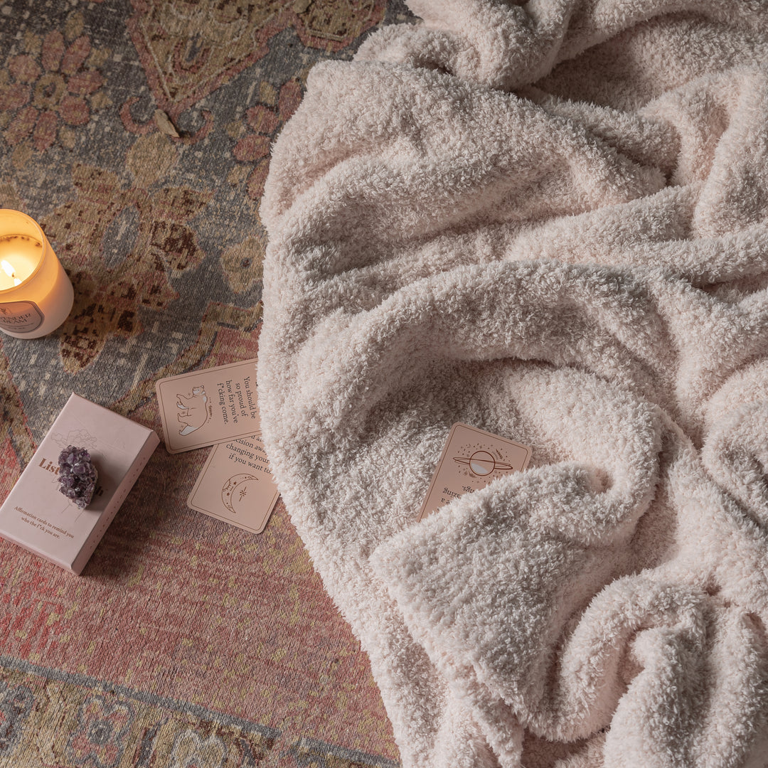 Cozy blanket draped over a textured surface with candles and cards.