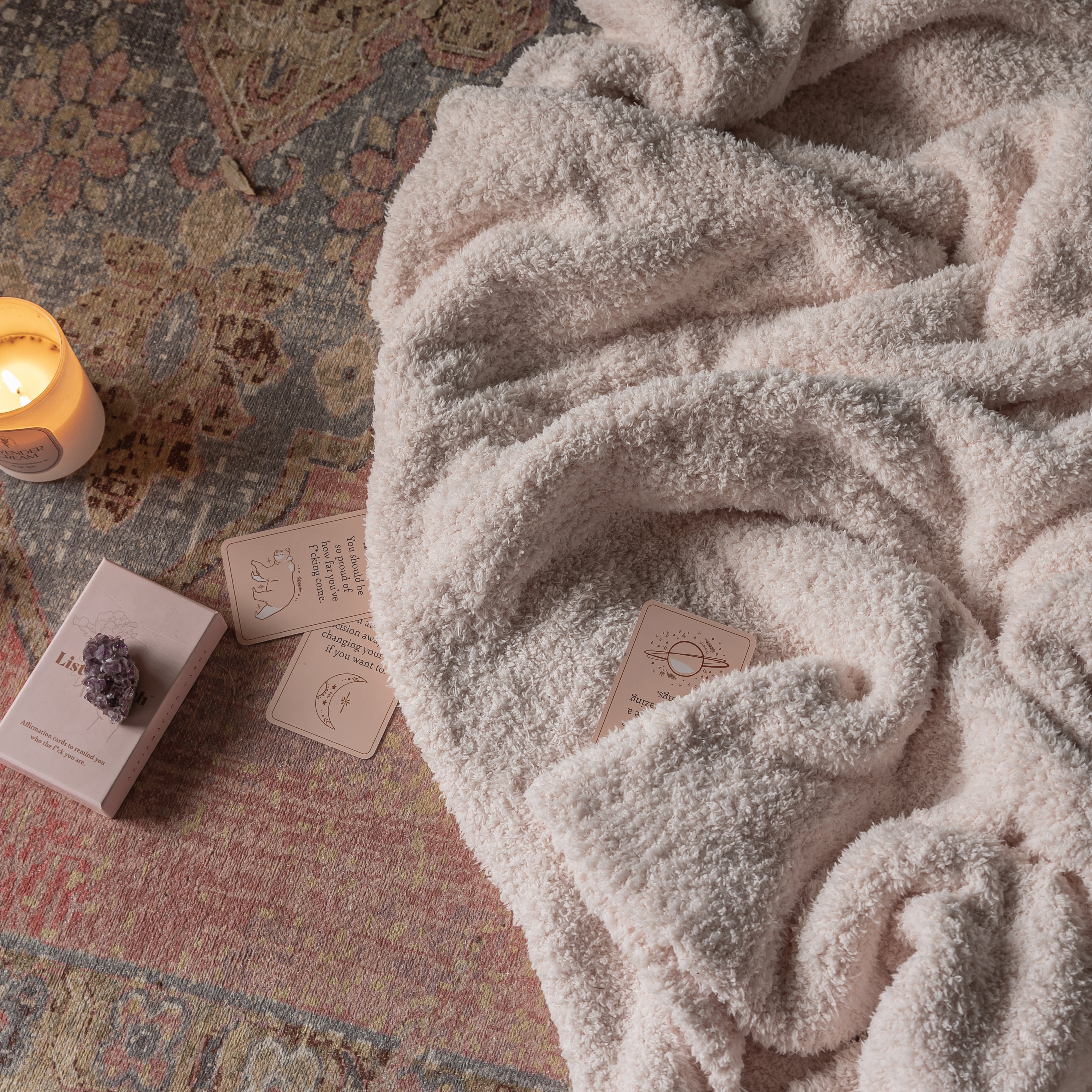 Cozy blanket draped over a textured surface with candles and cards.