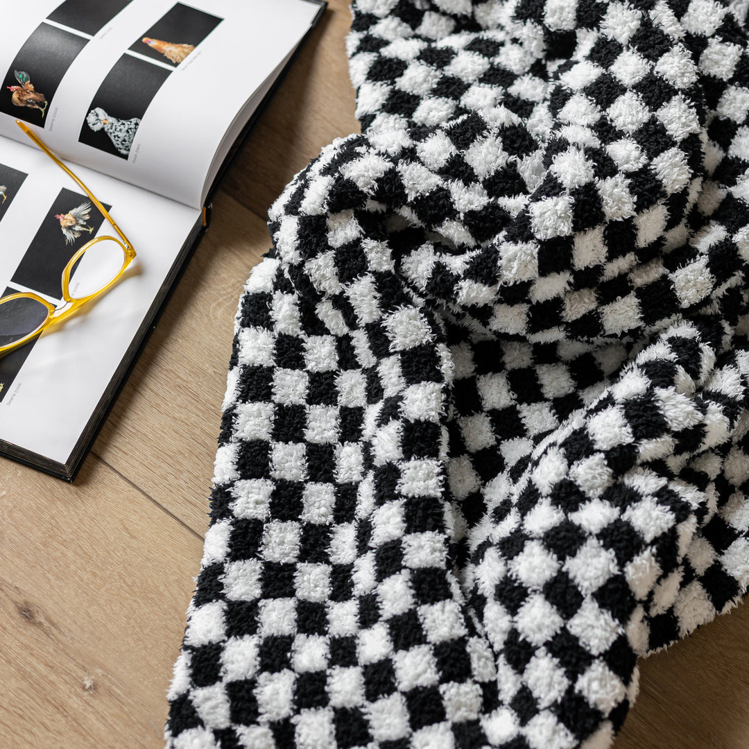 Black and white checkered blanket on a wooden surface with glasses and a magazine.