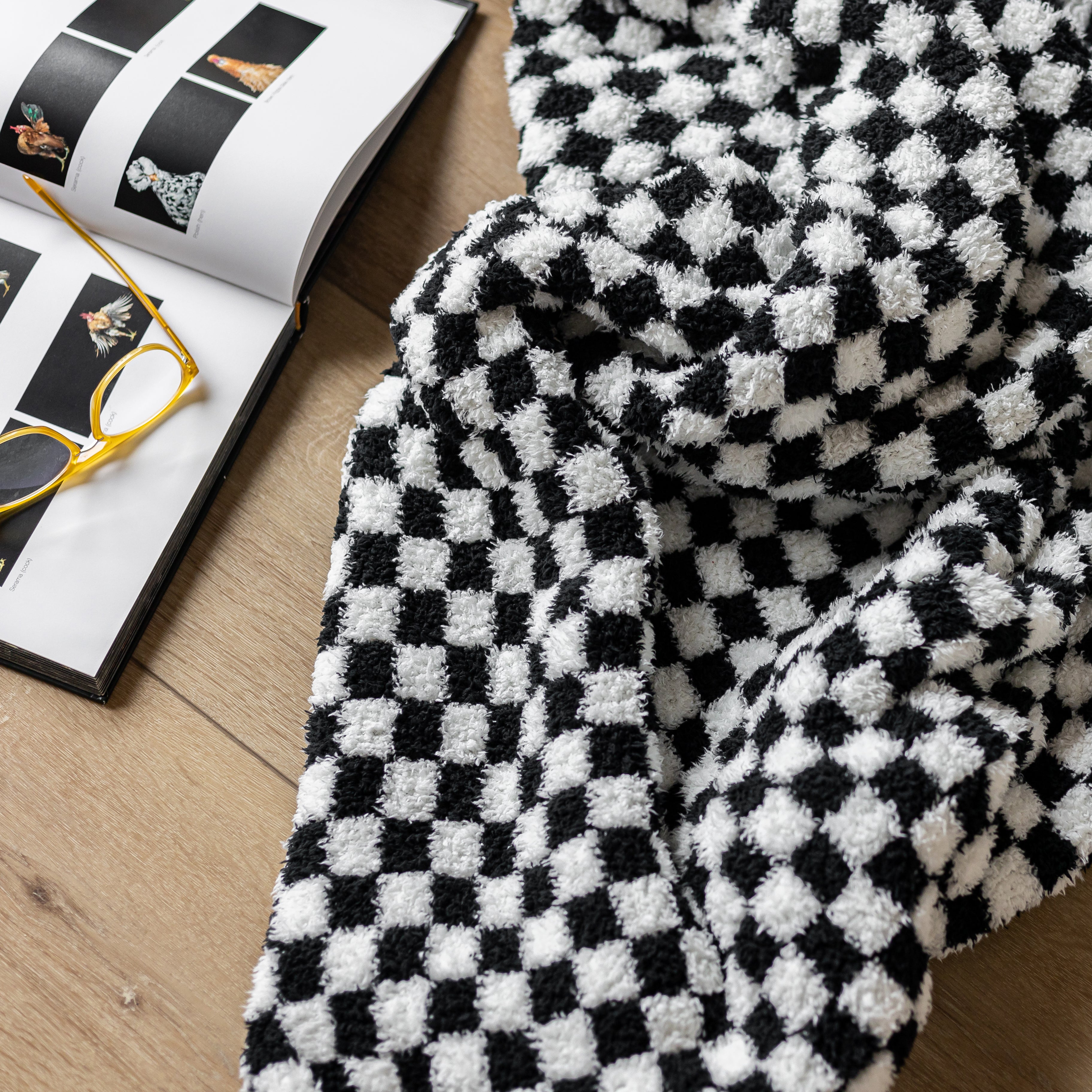 Black and white checkered blanket on a wooden surface with glasses and a magazine.