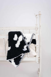 black and white cow print lovey baby blanket on a cradle