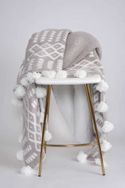 world's softest plush blanket in white and grey with tassels on stool